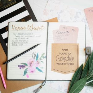 Flat lay of wedding planning materials including a journal, leaves, and stationery.